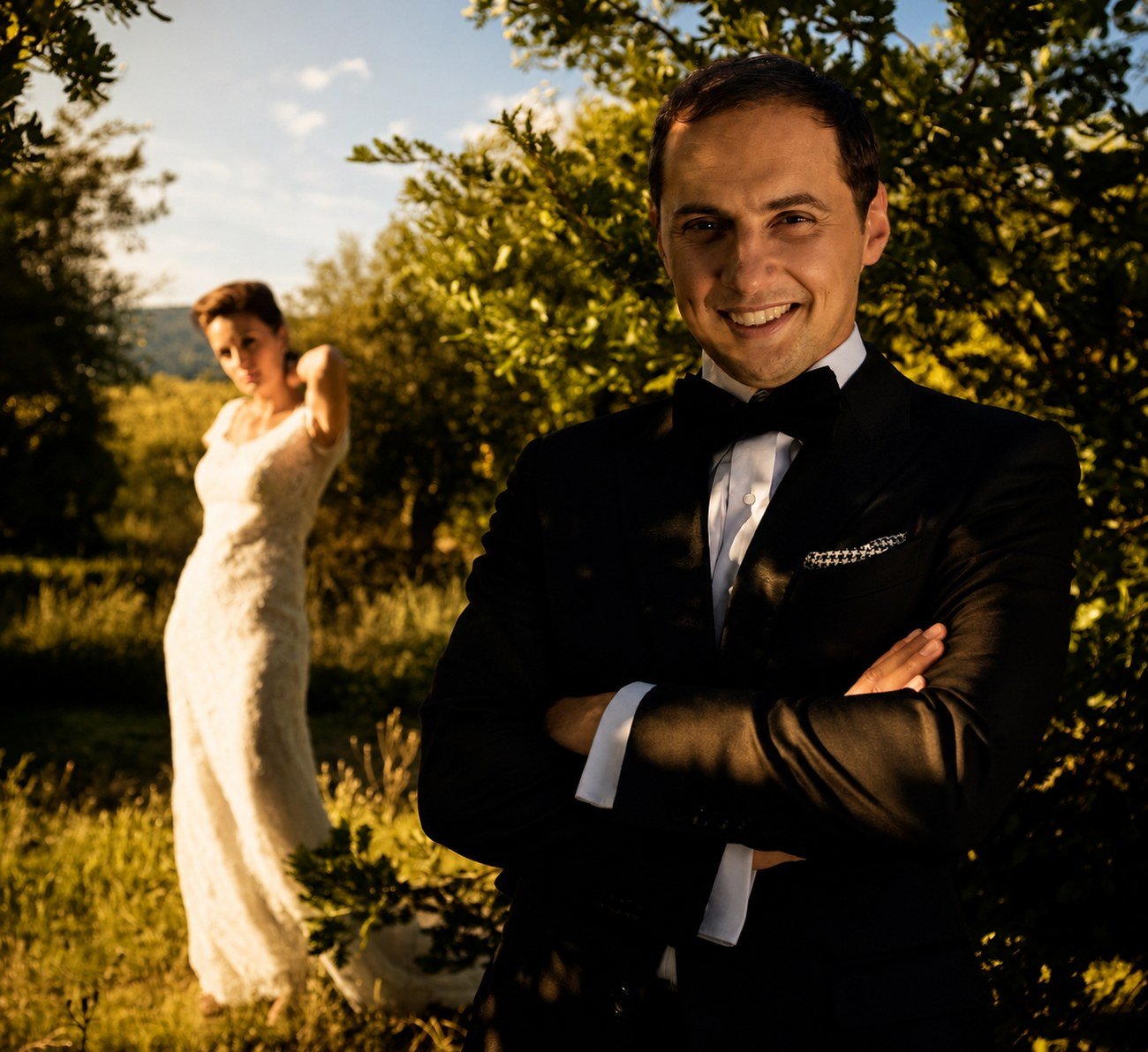 Groom portrait in the orchard, bride in the background